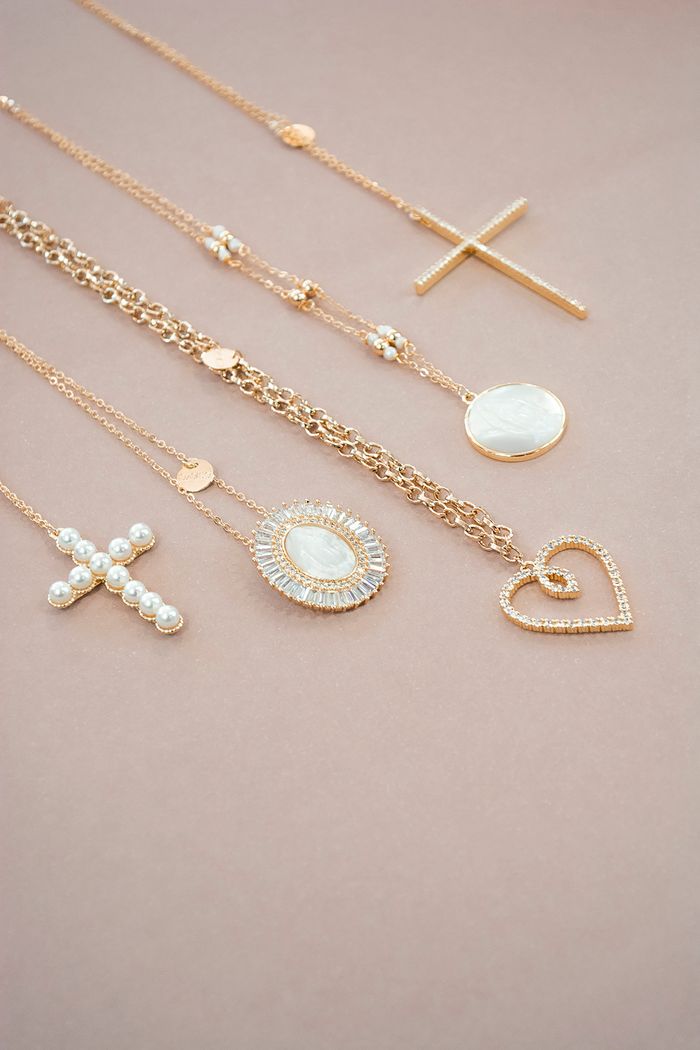 A collection of elegant gold necklaces and pendants artfully arranged on a soft pink background.